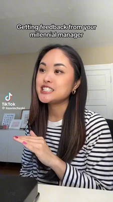 Vertical TikTok-style meme frame with the caption “Getting feedback from your millennial manager” centered near the top in large white text with a black outline. A woman with long dark hair, hoop earrings, and a black-and-white striped shirt sits indoors at a desk, facing slightly left. She holds one hand flat and palm-down in front of her while speaking, showing pink-painted nails and a tense, teeth-baring expression. Behind her are a light-colored wall, a white paneled door, and framed items on a cabinet. The TikTok logo and the text “TikTok” and “@lisavincheski” appear on the left. This meme is a video; captions are not available.